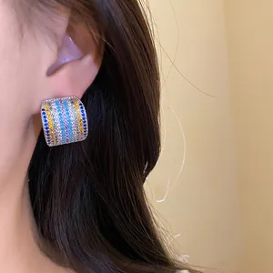 Detail close-up of a multi-colored zircon square stud earring worn on the ear