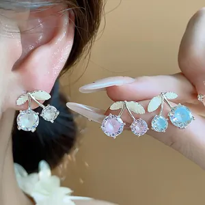 Detail of dainty zircon cherry stud earrings in pink, blue, and white sparkles.