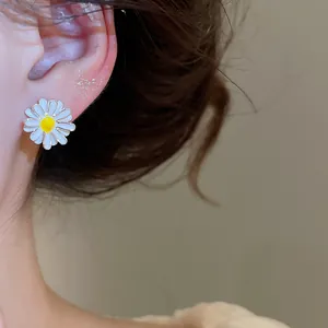 Close-up of a delicate white and yellow enamel daisy flower stud earring on ear