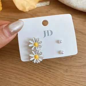 Detailed view of sweet white enamel daisy and small pearl stud earring set on a display card