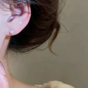 Elegant close-up detail of a minimalist small pearl stud earring worn on a model's ear.