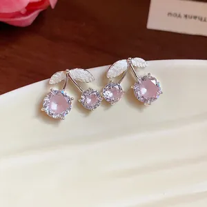Close-up of elegant pink zircon cherry stud earrings displayed on a white ceramic tray