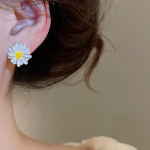 Close-up detail of a delicate white daisy enamel flower stud earring worn on a model's ear
