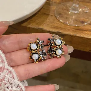 Orecchini a fiore dorati vintage con perle e cristalli mostrati su una mano