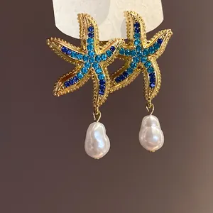 Close-up of elegant gold starfish earrings featuring blue rhinestones and baroque pearl drops