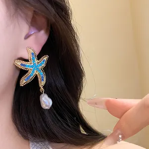 Close-up of gold starfish earrings with blue rhinestones and baroque pearl drop on ear.