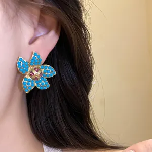 Macro detail of a gold starfish earring with blue beads and red center stones.