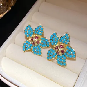 Macro detail of gold starfish stud earrings with turquoise beads and pink rhinestones.