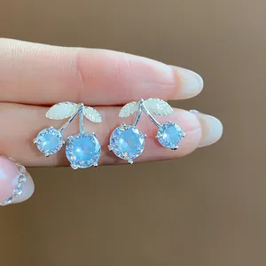Close-up of exquisite cherry stud earrings featuring light blue zircons and silver leaves