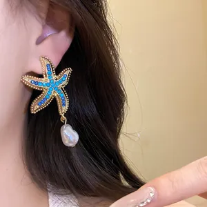 Detailed view of a gold starfish earring featuring blue crystals and a baroque pearl drop