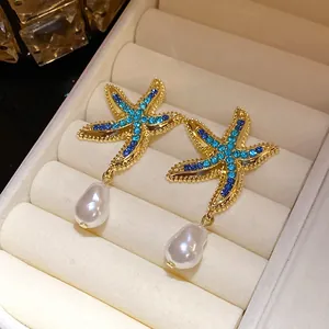 Detailed view of gold starfish earrings with blue rhinestones and dangling white pearls.