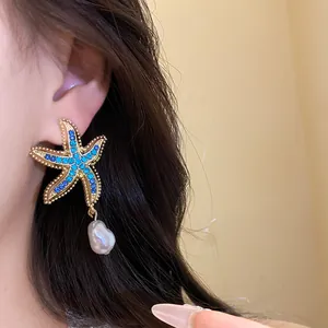 Close-up of elegant starfish earrings with blue rhinestones and baroque pearl dangles.