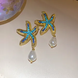 Close-up of gold starfish earrings with blue rhinestones and white teardrop pearls