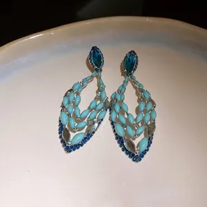 Close-up of bohemian hollow drop earrings with blue crystals and beads on silver needles.