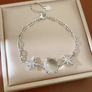 Close-up of an elegant silver-tone bracelet with star and round stone on a beige box.