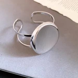 Vue détaillée d'un bracelet jonc ovale argenté minimaliste sur un fond gris texturé élégant