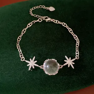 Detailed view of silver star bracelet with zircon and green glass stone on dark velvet