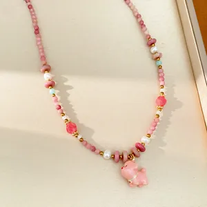 Close-up of a pink ceramic puppy charm on a beaded pearl necklace with golden accents.