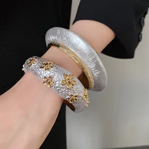 Detailed view of two textured metallic bangles with gold floral accents on a wrist.