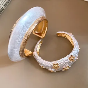 Detailed view of elegant white and gold metallic open cuff bracelets with floral texture