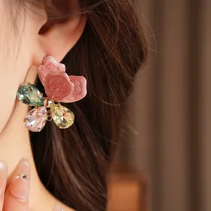 Close-up of elegant floral earrings with pink petals and colorful gemstones.
