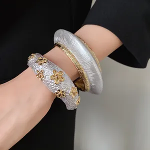 Detailed view of two chunky metallic cuff bangles with textured patterns and floral accents.
