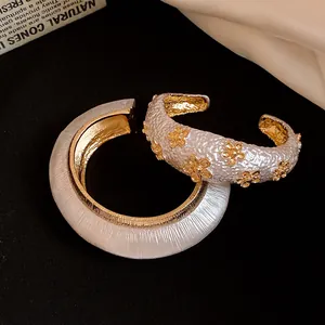 Detailed shot of white and gold textured metal open cuff bracelets with floral accents