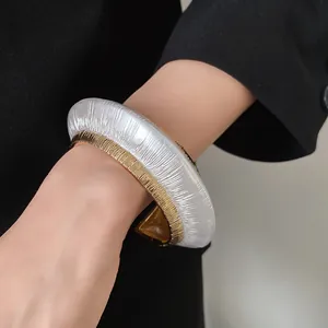 Close-up of a two-tone textured metal open cuff bracelet worn on a wrist.