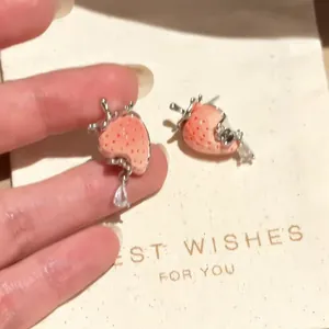 Close-up of cute strawberry enamel earrings with silver needle and teardrop crystal charm.