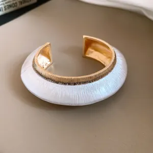 Macro view showing detailed white textured spray-paint and gold metal open cuff bracelet.