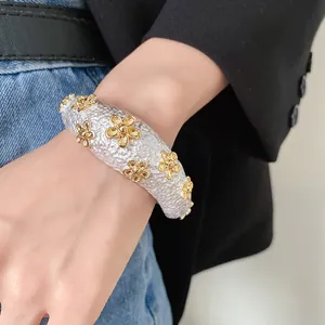 Close-up of textured silver cuff bracelet with gold flower details on female wrist