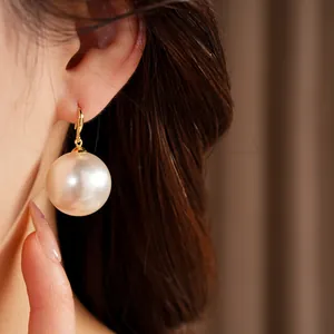 Detailed close-up showing an elegant large round pearl earring with 18k gold hook on model