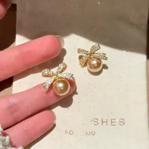 Detail view of gold-tone bow-knot stud earrings with pavé stones and golden pearls