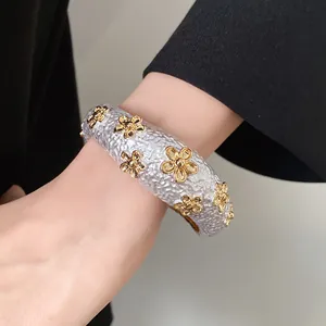 Elegant detail showing a silver textured open bangle with small golden flowers on wrist