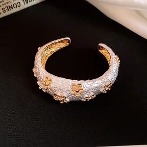 Close-up detail of white textured open bangle featuring delicate gold flower accents