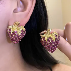 Vue macro détaillée de boucles d'oreilles fraises en strass violets portées à l'oreille