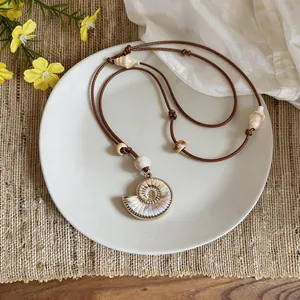 Close-up of a Bohemian spiral shell pendant necklace displayed on a white plate.