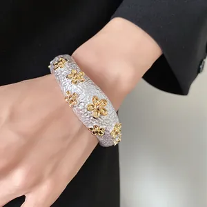 Detailed view of textured silver open bangle adorned with gold flower accents on a wrist