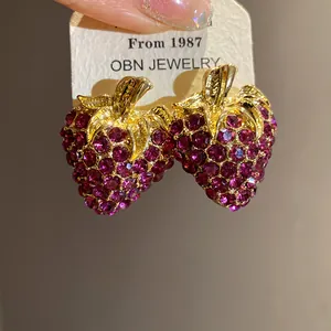 Détail de boucles d'oreilles fraise magenta étincelantes avec feuilles dorées