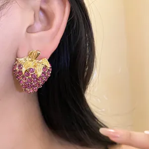 Gros plan détaillé de boucles d'oreilles fraises en strass roses portées à l'oreille.