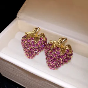 Gros plan de boucles d'oreilles fraises plaquées or avec des strass violets fins