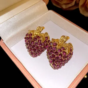 Gros plan détaillé de boucles d'oreilles fraises avec strass violets dans une boîte