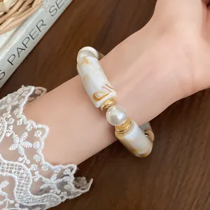 Detail view of a marble acrylic bracelet with gold accents and a white pearl.