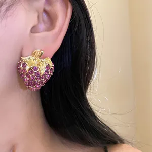 Gros plan d'une boucle d'oreille fraise étincelante en strass violets sur l'oreille