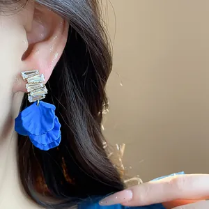 Primo piano di orecchini a petalo blu Klein con zirconi indossati da una modella