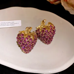 Vue détaillée de boucles d'oreilles fraises en strass violets sur un plateau blanc