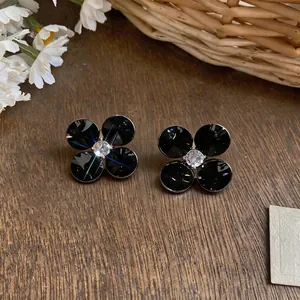 Elegant black flower stud earrings with sparkling crystal center on a rustic wooden background