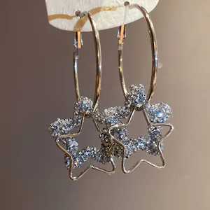Macro view of textured glittering resin star pendant silver needle hoop earrings