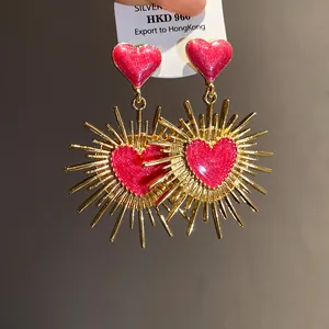 Gros plan sur les boucles d'oreilles vintage avec cœur en émail rose et rayons dorés.