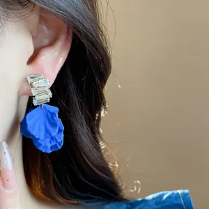 Dettaglio ravvicinato di orecchini a petalo in acrilico blu Klein con zirconi lucidi.